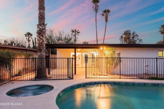 back of house at dusk featuring a fenced in pool, brick siding, a chimney, fence, and an in ground hot tub