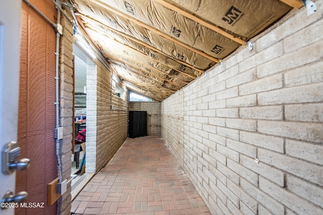 corridor with lofted ceiling, brick wall, and brick floor