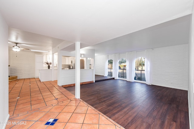 unfurnished living room featuring ceiling fan, brick wall, and wood finished floors