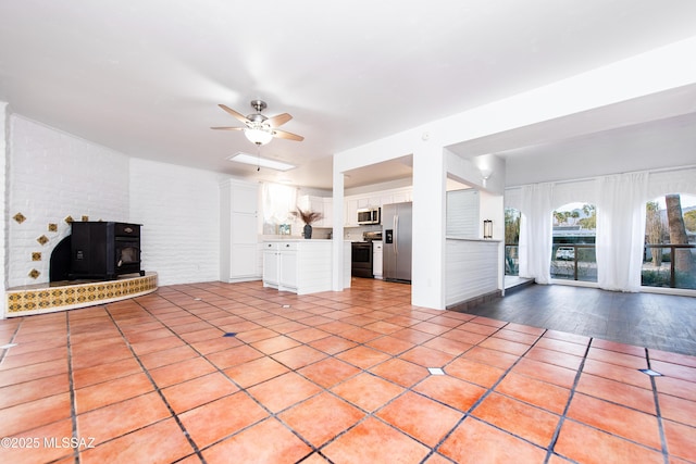 unfurnished living room with light tile patterned floors, ceiling fan, and a wood stove