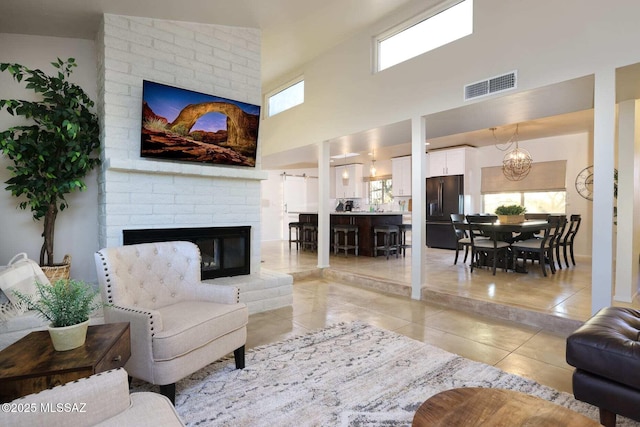 living area featuring light tile patterned floors, a chandelier, a high ceiling, a fireplace, and visible vents