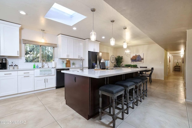 kitchen featuring an island with sink, light countertops, white cabinets, a skylight, and black appliances