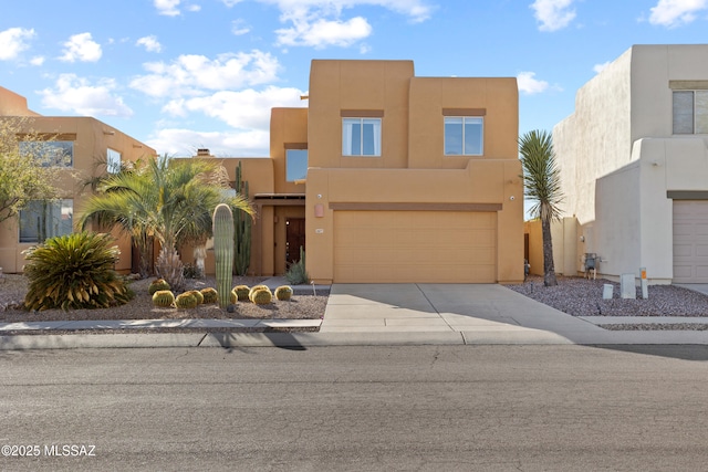 pueblo-style house featuring stucco siding, driveway, and a garage