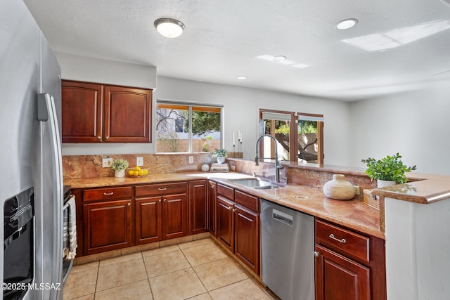 kitchen with dark brown cabinets, light tile patterned floors, appliances with stainless steel finishes, a peninsula, and a sink