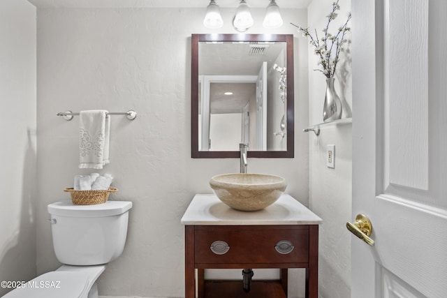 half bathroom with visible vents, toilet, vanity, and a textured wall