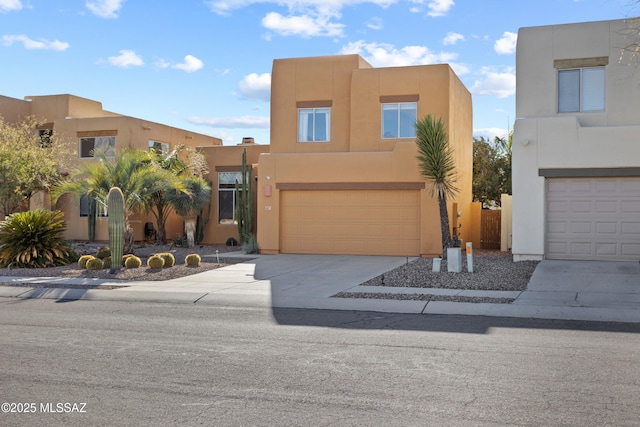 pueblo revival-style home with a garage, stucco siding, and driveway