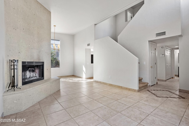 unfurnished living room featuring stairway, visible vents, a high end fireplace, tile patterned flooring, and a notable chandelier