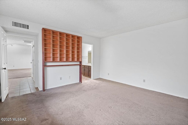 unfurnished living room featuring light carpet, light tile patterned floors, a textured ceiling, and visible vents