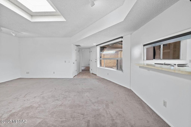 empty room featuring carpet floors, a skylight, baseboards, and a textured ceiling