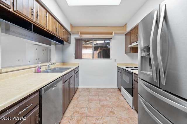 kitchen featuring baseboards, appliances with stainless steel finishes, light countertops, under cabinet range hood, and a sink