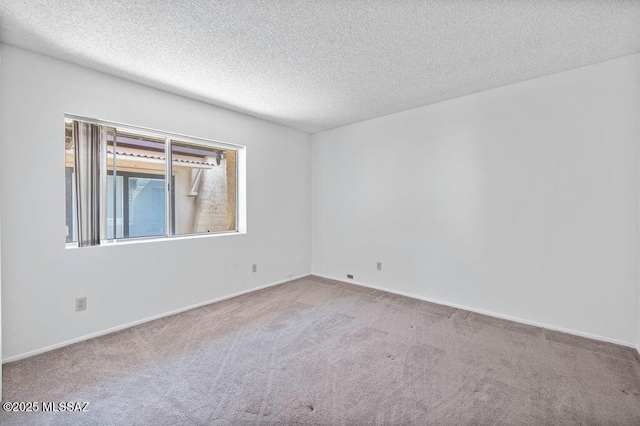 carpeted spare room featuring a textured ceiling and baseboards