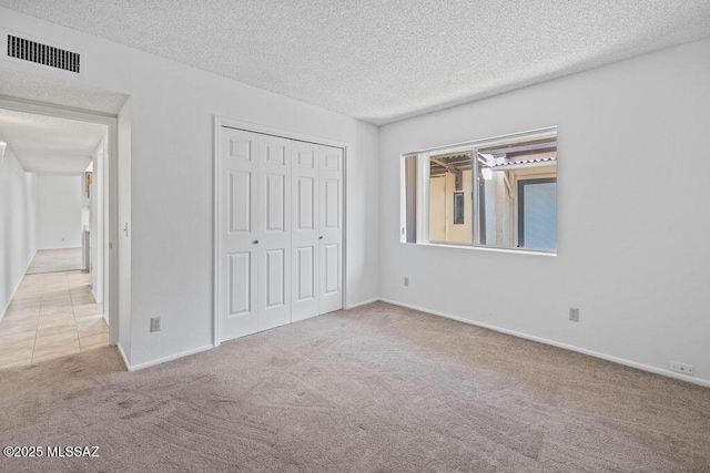 unfurnished bedroom featuring baseboards, visible vents, carpet, a textured ceiling, and a closet