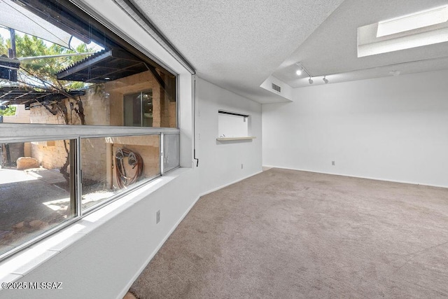 empty room featuring visible vents, carpet flooring, a textured ceiling, track lighting, and baseboards