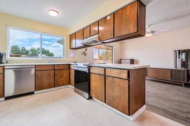 kitchen with under cabinet range hood, stainless steel appliances, a peninsula, light countertops, and brown cabinetry