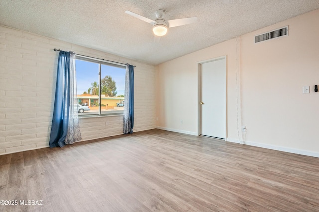 spare room with a textured ceiling, wood finished floors, visible vents, and a ceiling fan