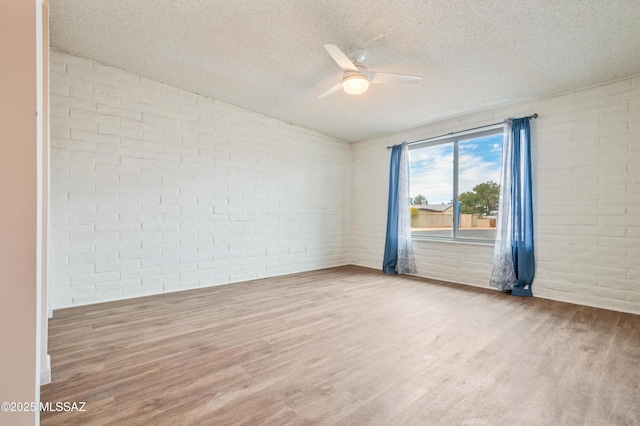 spare room featuring a ceiling fan, a textured ceiling, brick wall, and wood finished floors