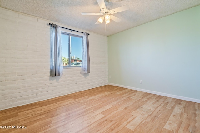 empty room featuring a ceiling fan, a textured ceiling, brick wall, wood finished floors, and baseboards