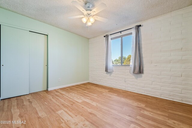 unfurnished bedroom with light wood finished floors, a closet, ceiling fan, a textured ceiling, and brick wall