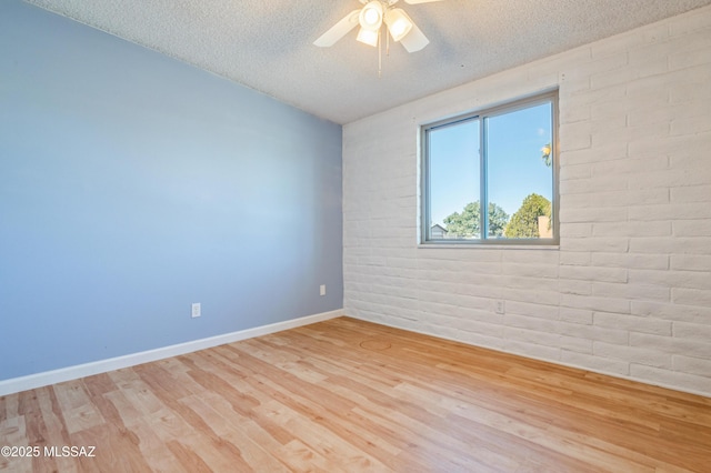 unfurnished room featuring a textured ceiling, brick wall, wood finished floors, a ceiling fan, and baseboards