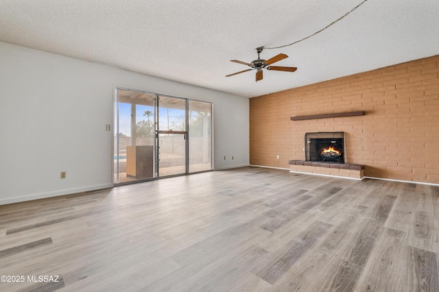 unfurnished living room featuring a textured ceiling, ceiling fan, a fireplace, wood finished floors, and baseboards