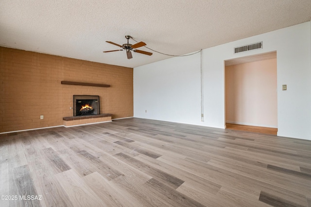 unfurnished living room with a textured ceiling, a fireplace, wood finished floors, visible vents, and a ceiling fan