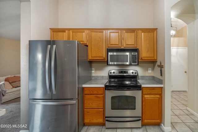 10117 E Sky Castle Way, Tucson, AZ 85730 - kitchen featuring light countertops, stainless steel appliances, light tile patterned flooring, arched walkways, and brown cabinetry