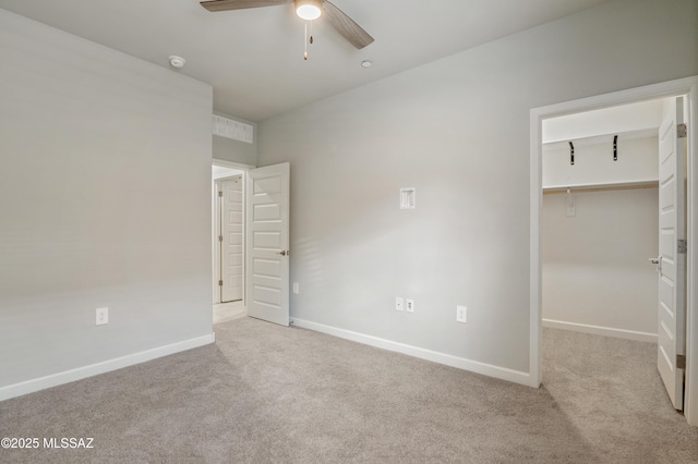 unfurnished bedroom with carpet flooring, ceiling fan, a walk in closet, and baseboards