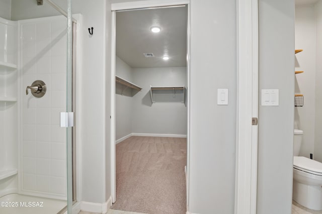 bathroom featuring visible vents, a walk in closet, baseboards, toilet, and a stall shower