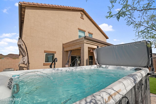 back of property with fence, a hot tub, and stucco siding