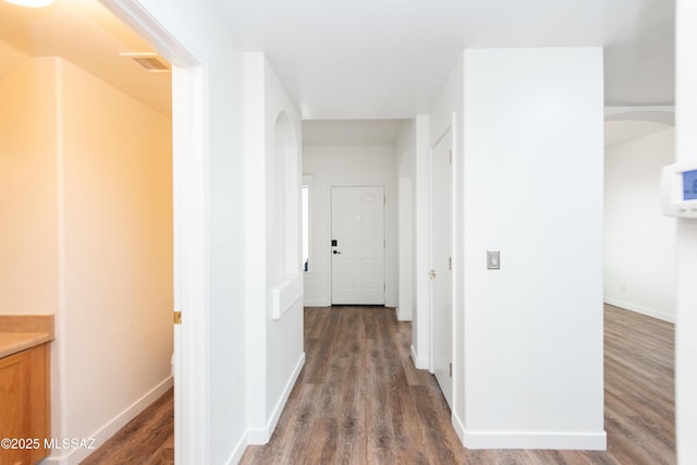 hallway with arched walkways, visible vents, baseboards, and wood finished floors