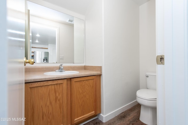 half bath with baseboards, visible vents, toilet, wood finished floors, and vanity