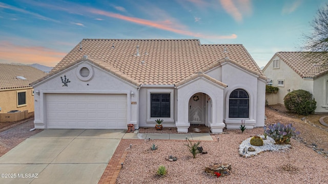 view of front of home featuring stucco siding, a tiled roof, an attached garage, and driveway