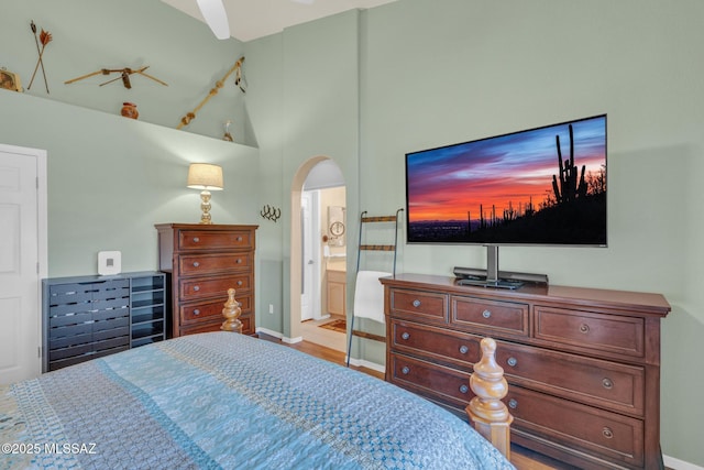 bedroom with arched walkways, high vaulted ceiling, ensuite bathroom, and baseboards