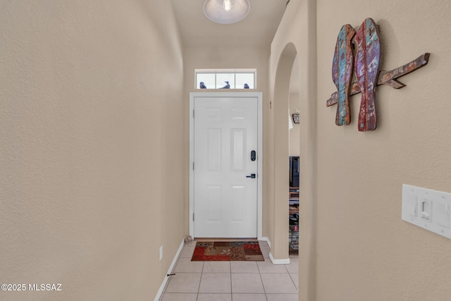 doorway to outside featuring light tile patterned floors, arched walkways, and baseboards