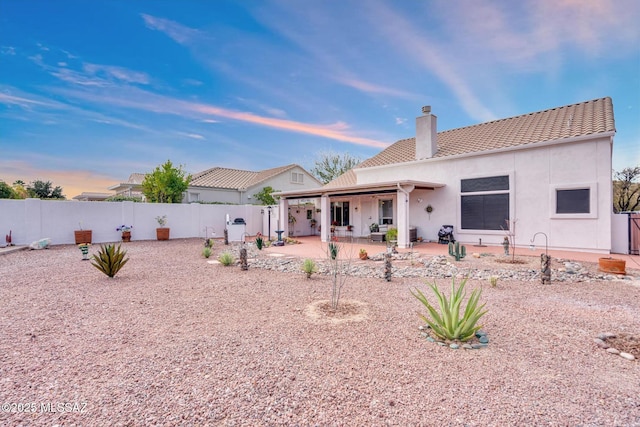 rear view of property with a tiled roof, stucco siding, a chimney, a fenced backyard, and a patio area