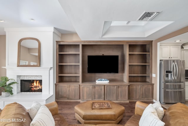 living room featuring visible vents, a warm lit fireplace, and wood finished floors