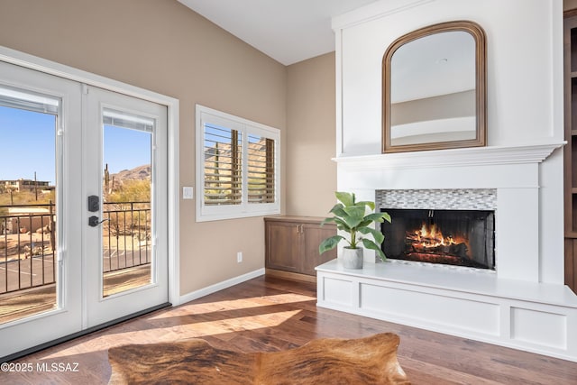 living area with a tiled fireplace, french doors, baseboards, and wood finished floors