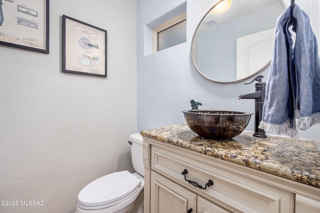 half bath featuring toilet, vanity, and a textured wall