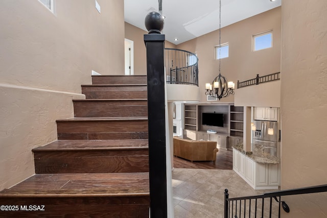 staircase featuring a high ceiling, an inviting chandelier, and a textured wall