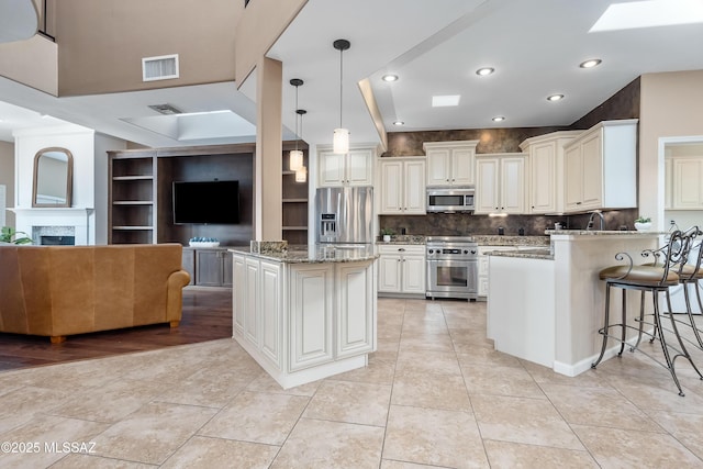 kitchen featuring visible vents, open floor plan, light stone counters, a peninsula, and stainless steel appliances