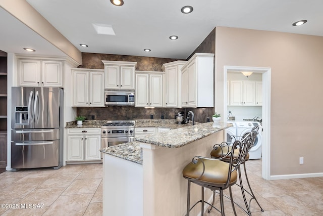 kitchen with light stone counters, a breakfast bar, a peninsula, stainless steel appliances, and washer and clothes dryer