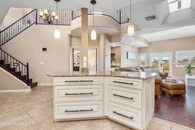 kitchen featuring visible vents, a notable chandelier, light stone counters, cream cabinets, and open floor plan