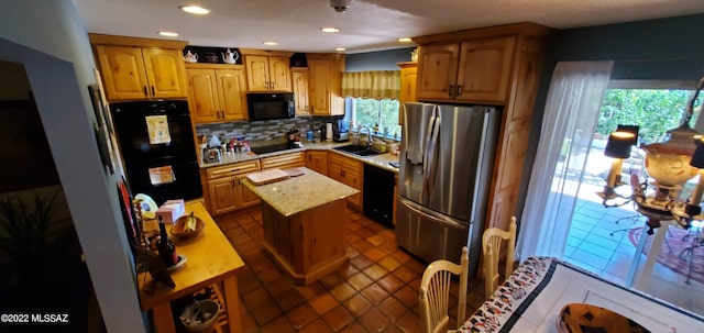 kitchen with light stone countertops, a sink, a center island, decorative backsplash, and black appliances