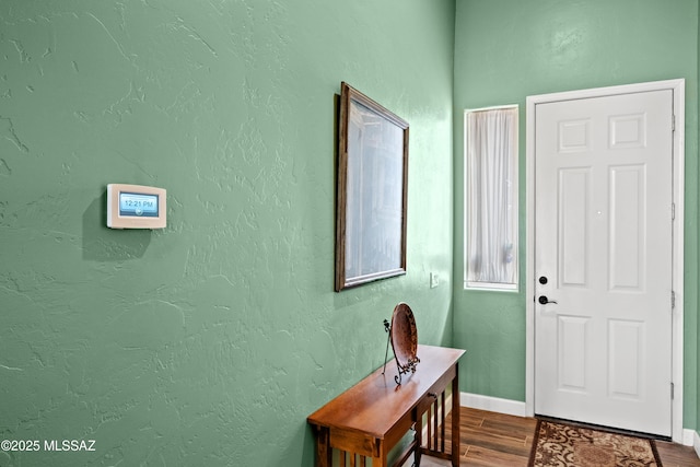 entryway with dark wood-style flooring, a textured wall, and baseboards