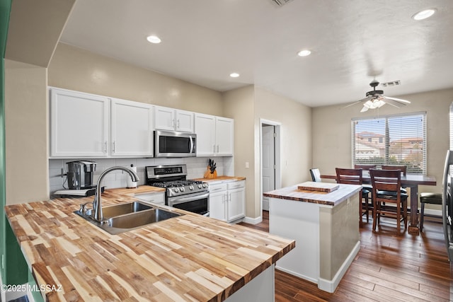 kitchen featuring stainless steel appliances, butcher block counters, a sink, white cabinets, and decorative backsplash