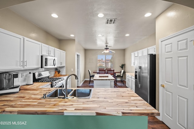 kitchen with a peninsula, a sink, wood counters, visible vents, and appliances with stainless steel finishes