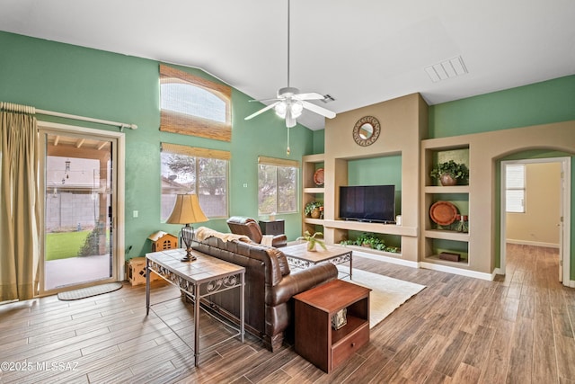 living area with built in features, arched walkways, visible vents, and wood finished floors