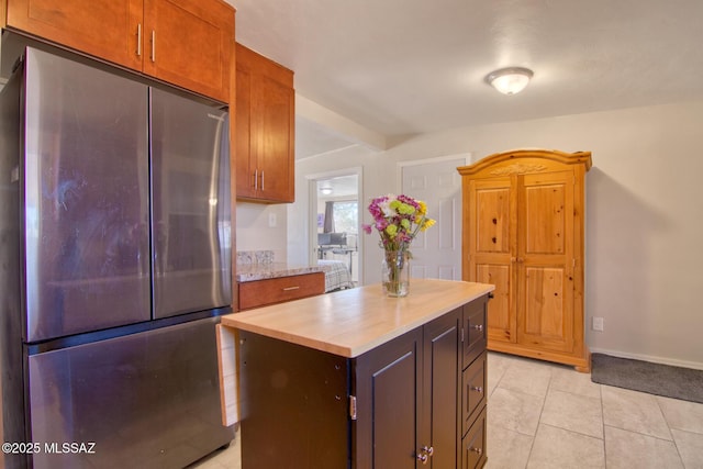 kitchen with light tile patterned floors, a kitchen island, baseboards, freestanding refrigerator, and brown cabinetry