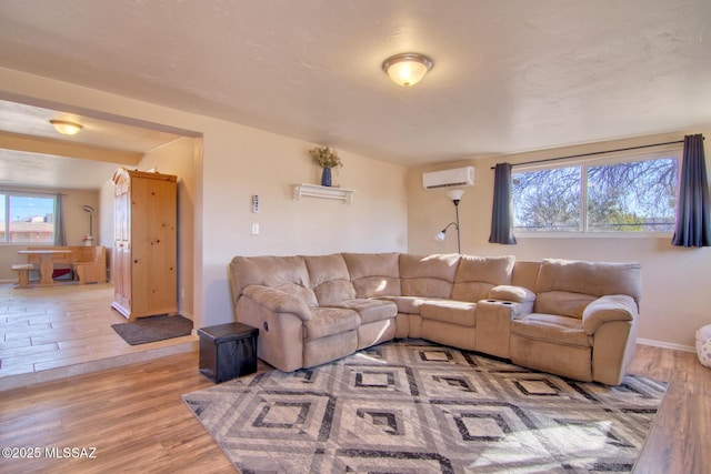 living room featuring light wood-style flooring, baseboards, and a wall mounted AC