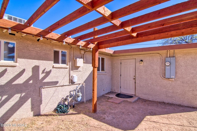 entrance to property with electric panel, stucco siding, and a pergola